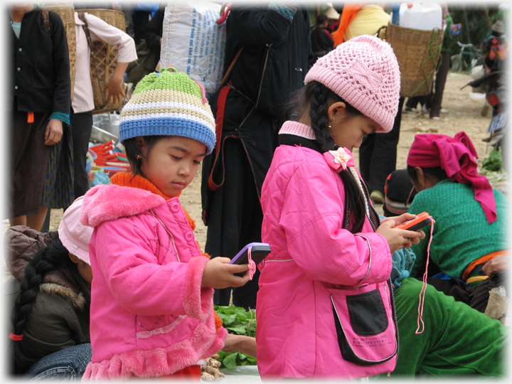 Two small girls in pink next to one another looking at pink phones.