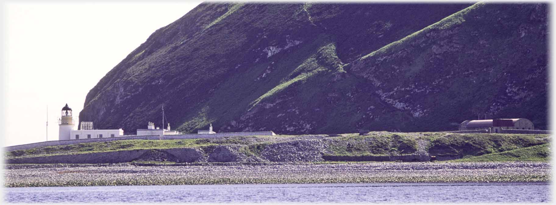 Lighthouse on shore under hill.