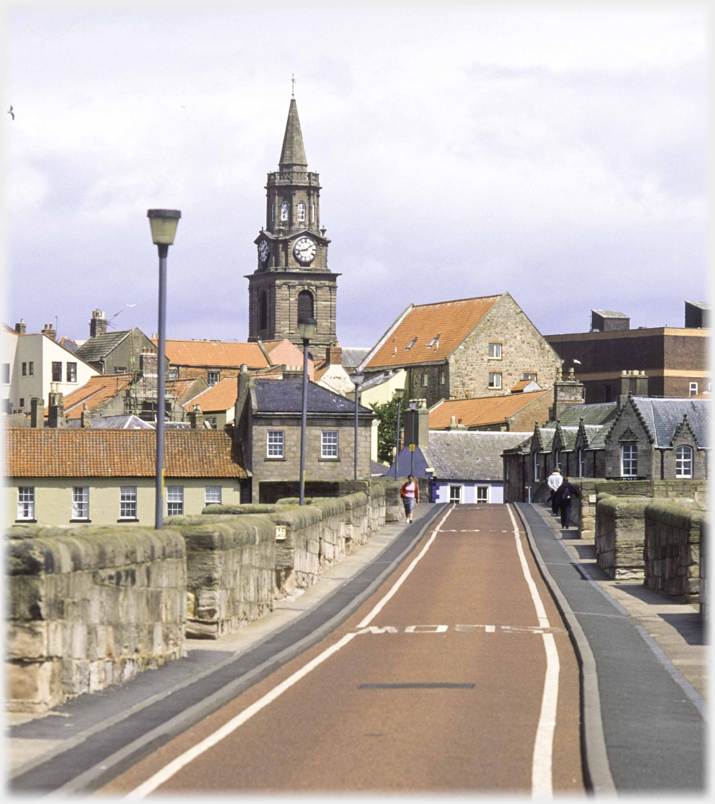 View along narrow parapeted bridge with buildings ahead.