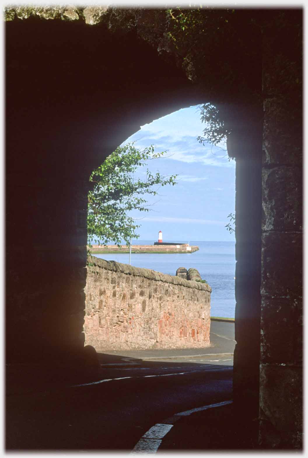 Road through wall with pier and lighthouse framed.