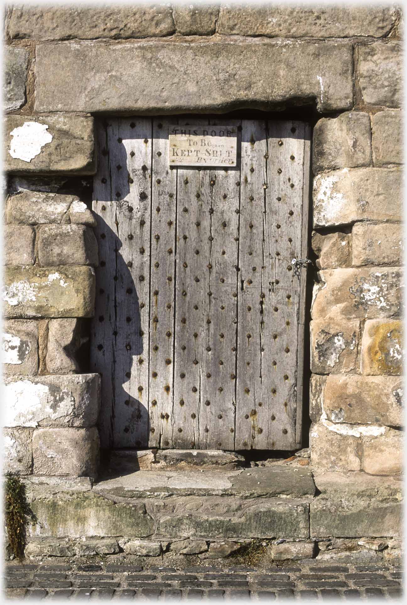 Studded wooden door in wall with sign at top saying This door to be kept shut.