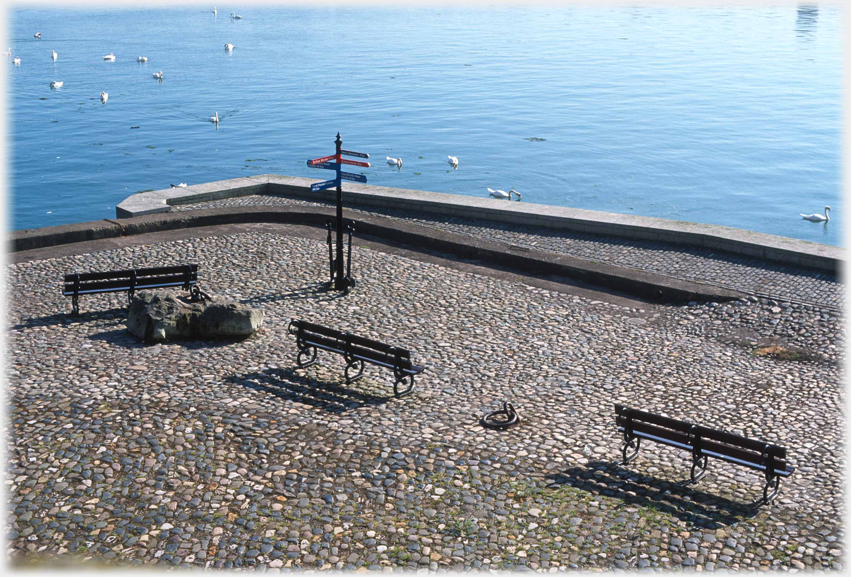 Cobbled promanade with benches and sea around.