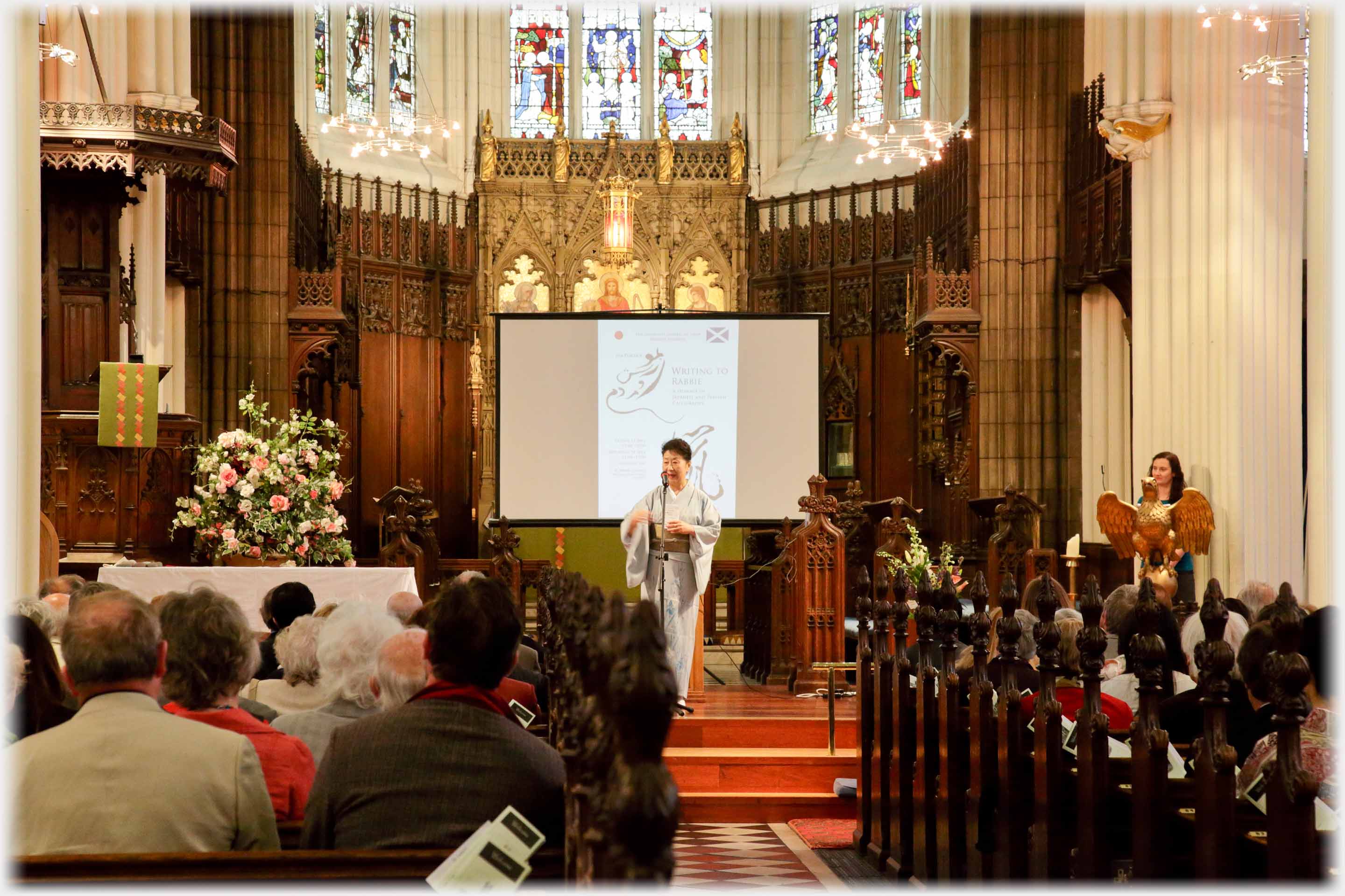 Woman in kimono at microphone in front of audience in church.