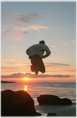 Figure jumping over sunset between rocks.
