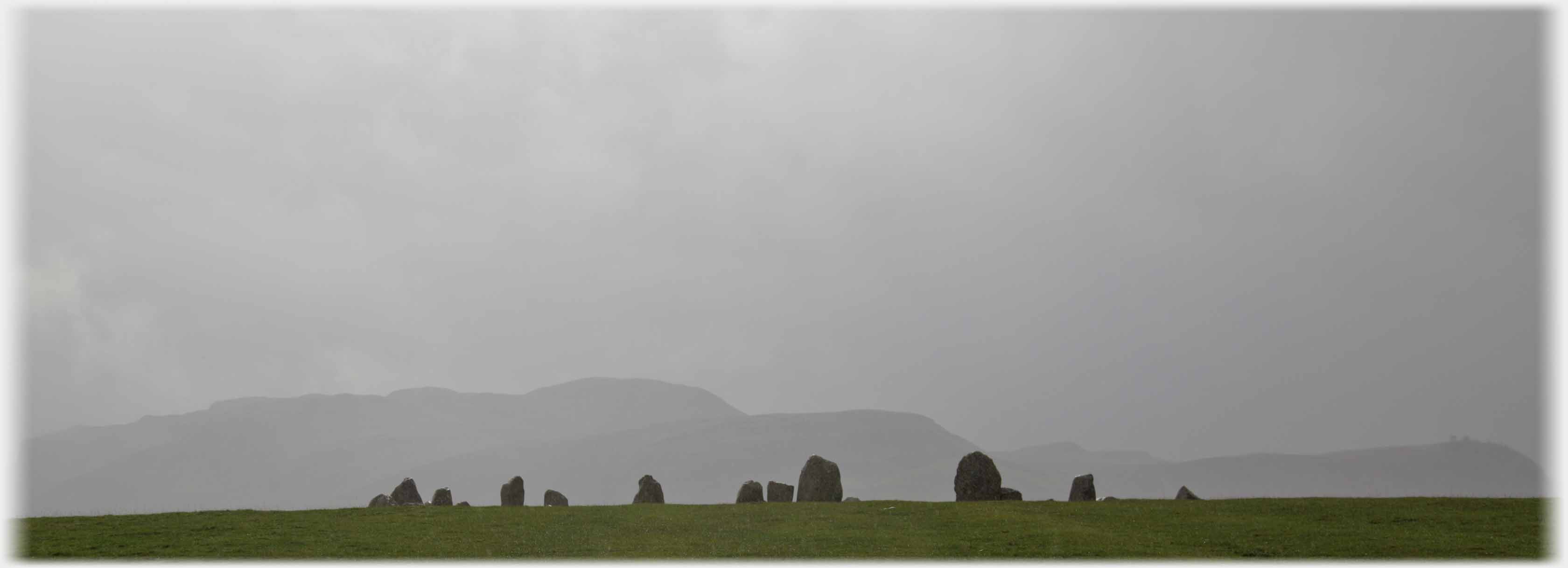 Line of black stones against deep grey cloud and hill.