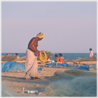 Man coiling rope amongst piles of nets.