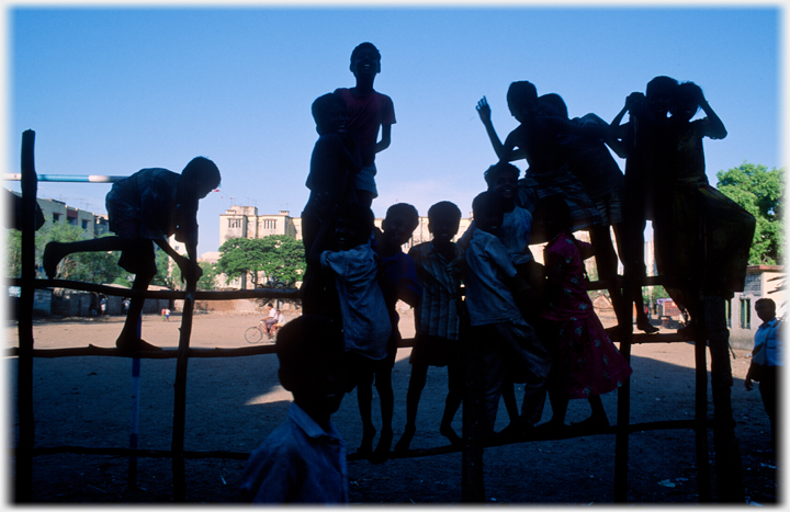 Silhouttes of children playing on a fence.