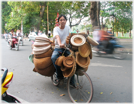 Hawker on bicycle with many baskets amongst traffic in Ha Noi.