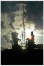 Works superstructures shrouded in steam, sun behind.