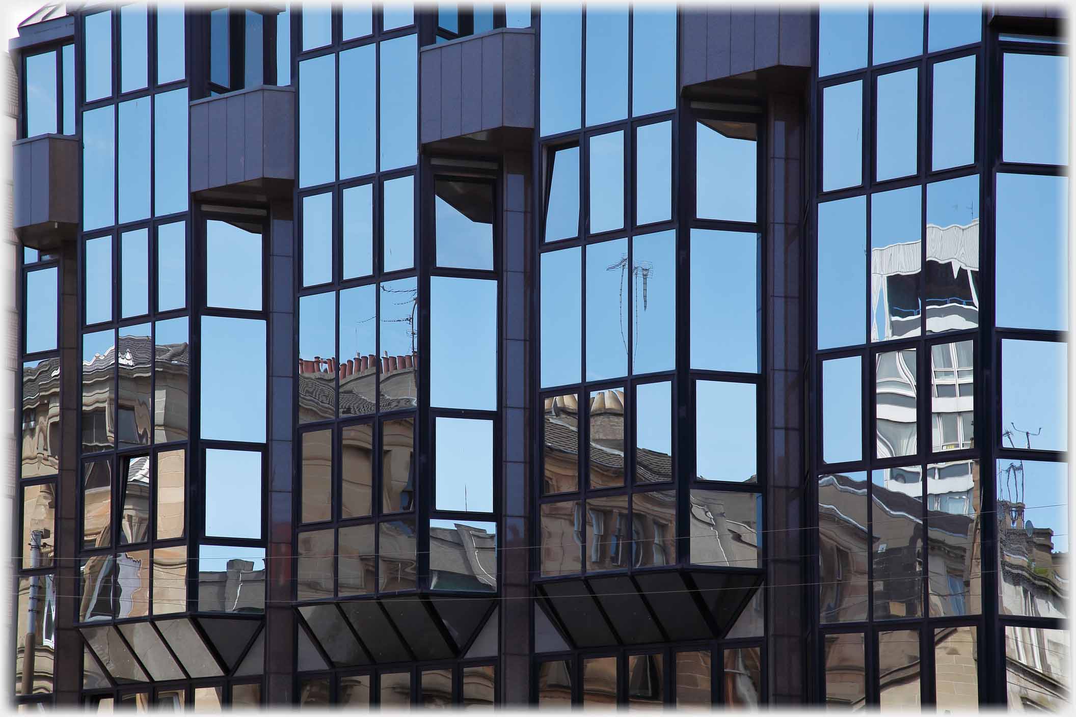 Glass fronted building with reflections of blue sky and older buildings.