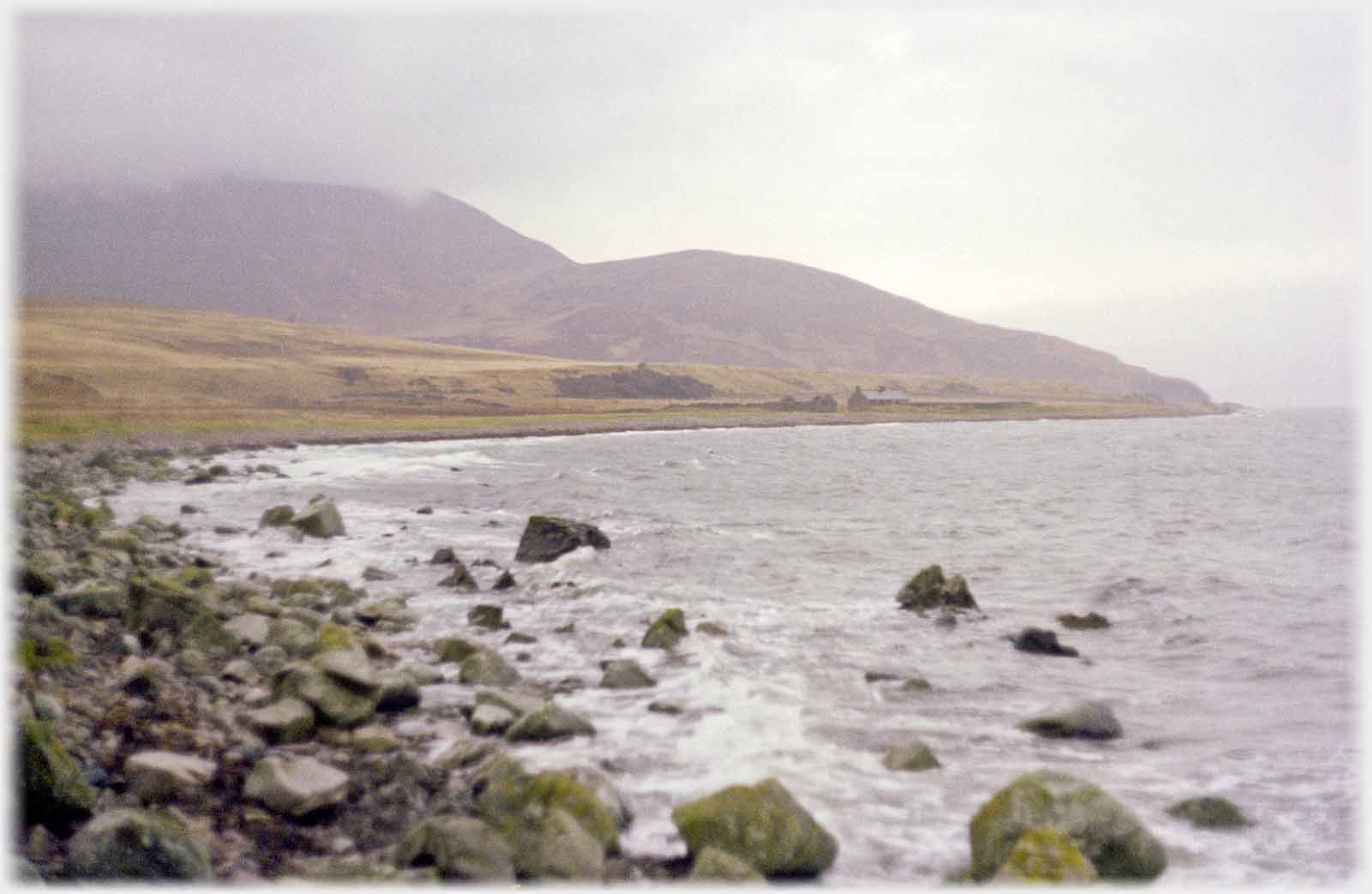 Soft shot of shore, distant building, with low cloud.