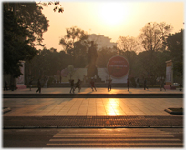 Silhouetted figues on low paved area with rising sun and statue behind.