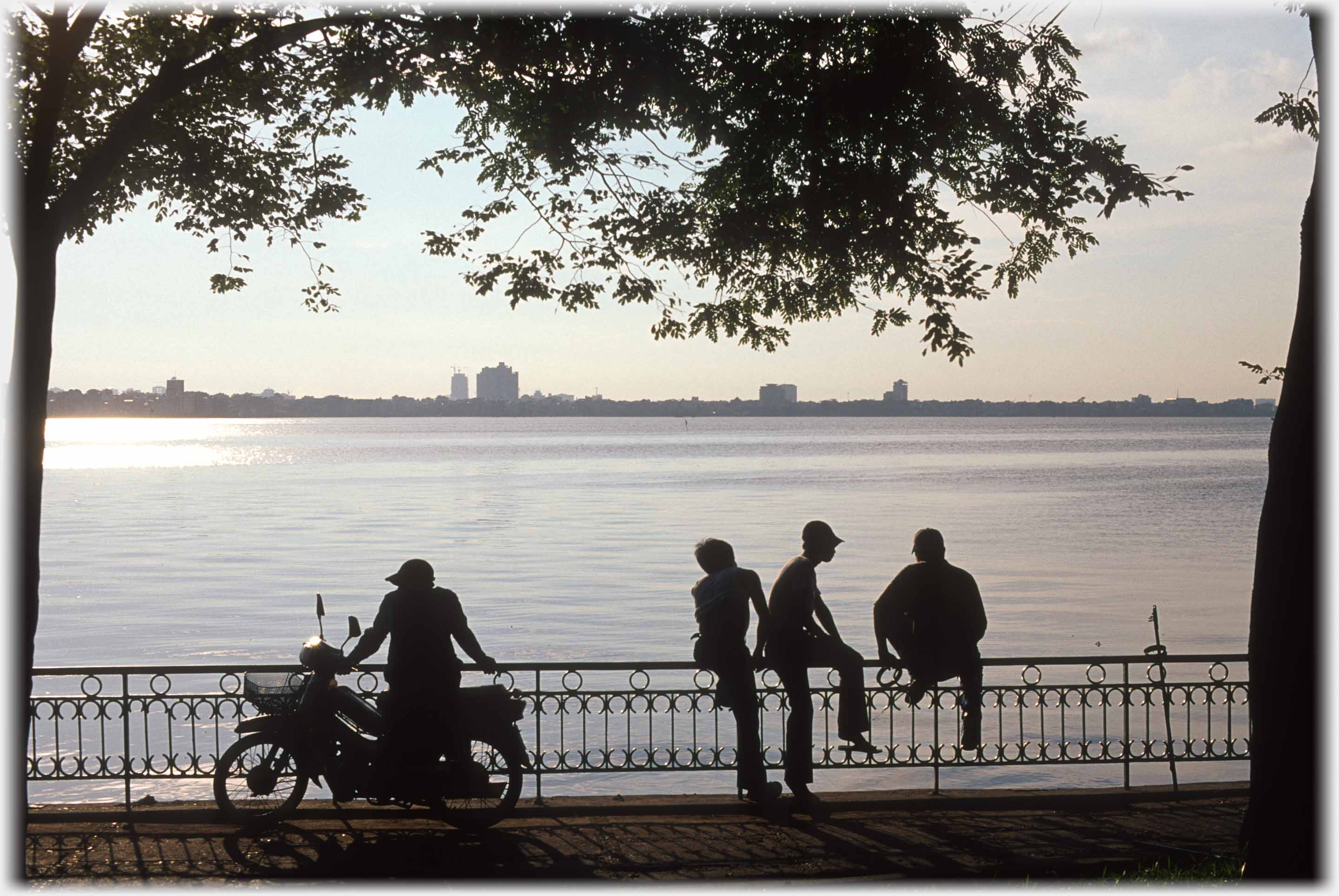 Silhouette of group sitting railings by lake.