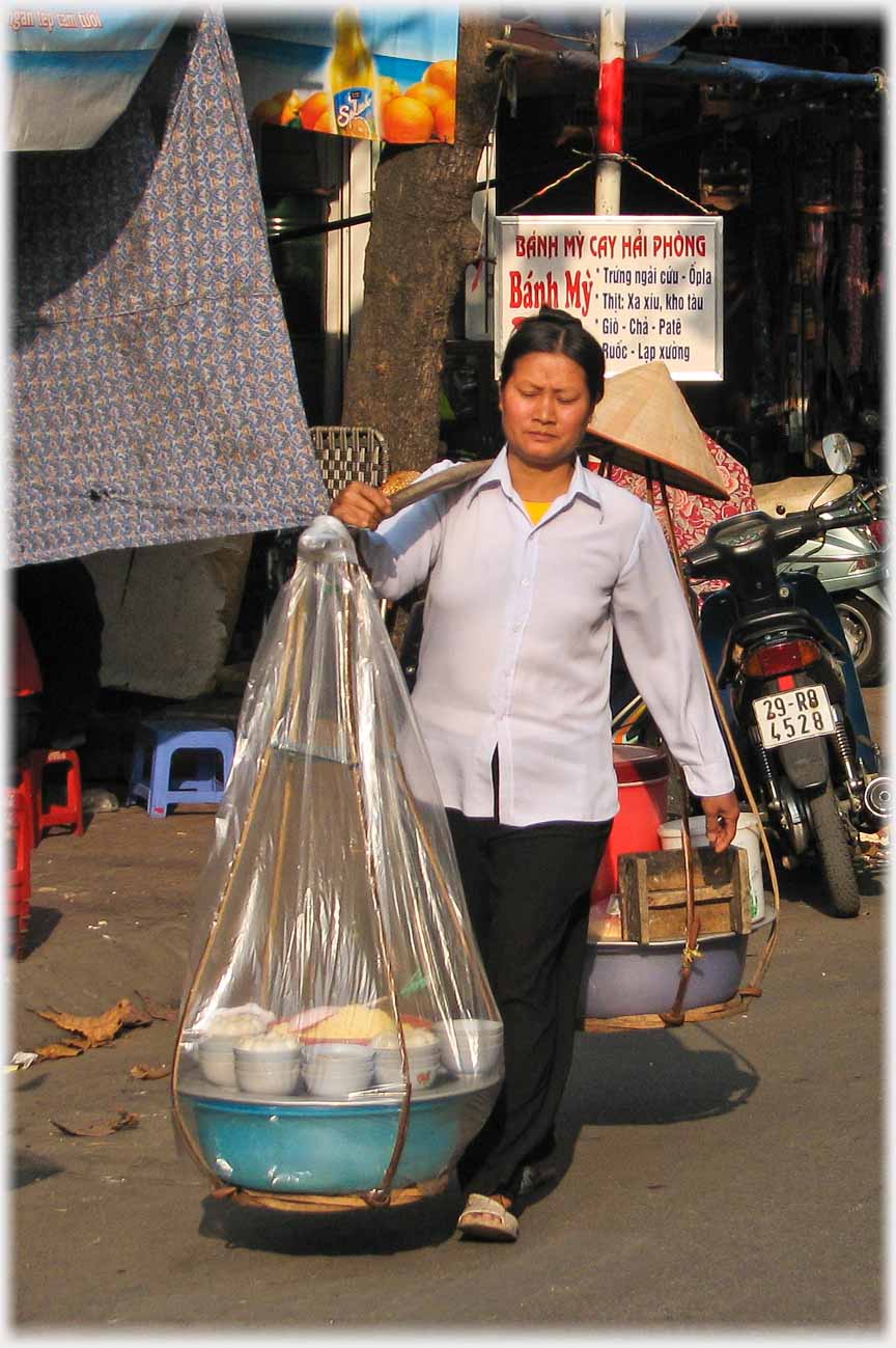 Woman walking carrying pannier with food and bowls visible through plastic.