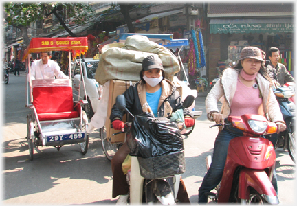 Woman with load on motorbike, empty rickshaw following.