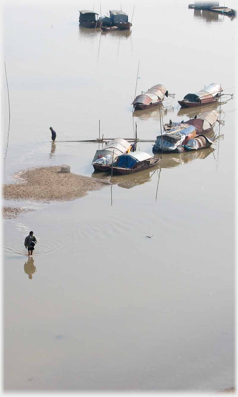 Group of houseboats in shallow water with two men walking in the water.
