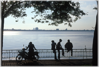 Silhouettes of four men sitting on railings by lake.