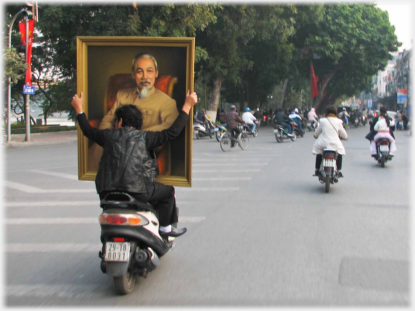 Motorbike pillion holding very parge portait of Uncle Ho.