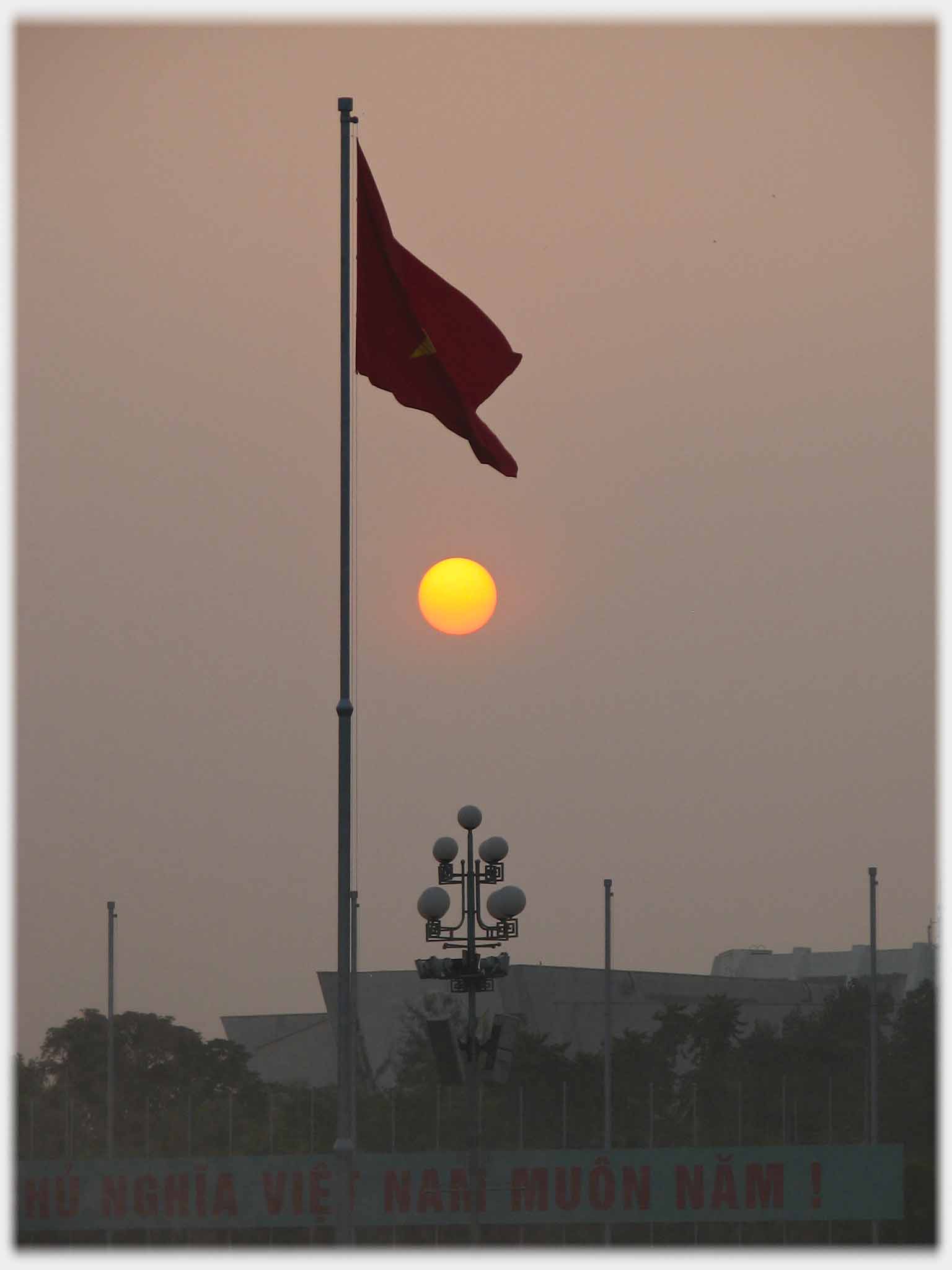 Flag embracing disc of setting sun.
