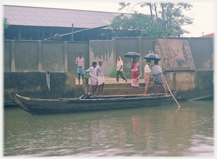 People standing by punt on steps by river, factory behind.