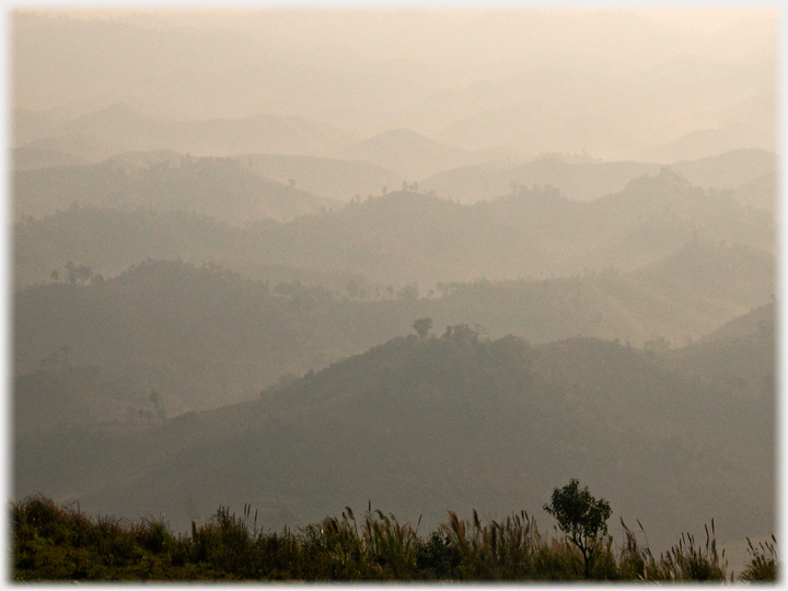 A light mist lying in valleys in wave after wave of tree-clad hills .