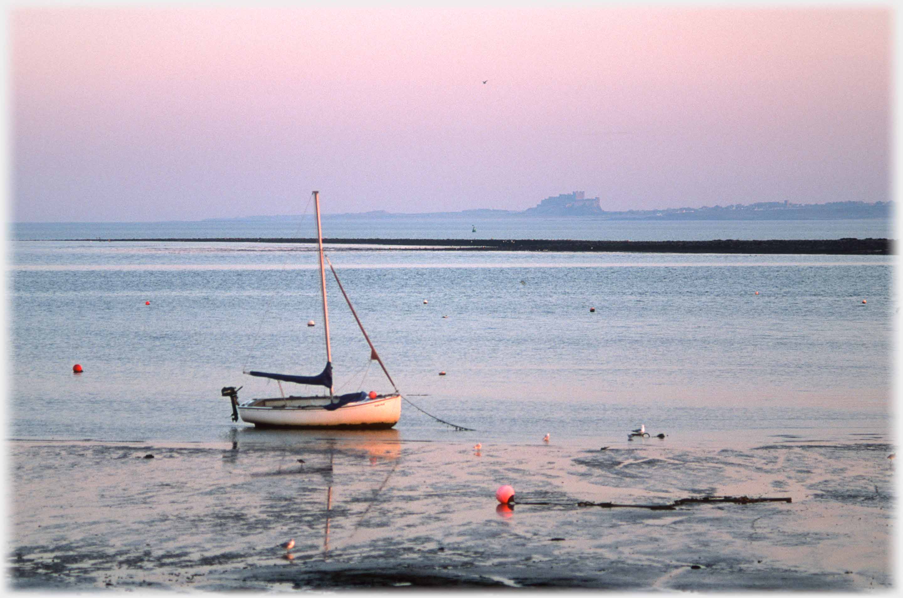 Small dinghy on sand at edge of sea with distant castle.