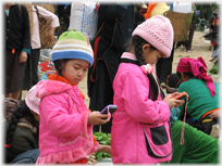 Two girls in pink clothes, looking at two pink phones.