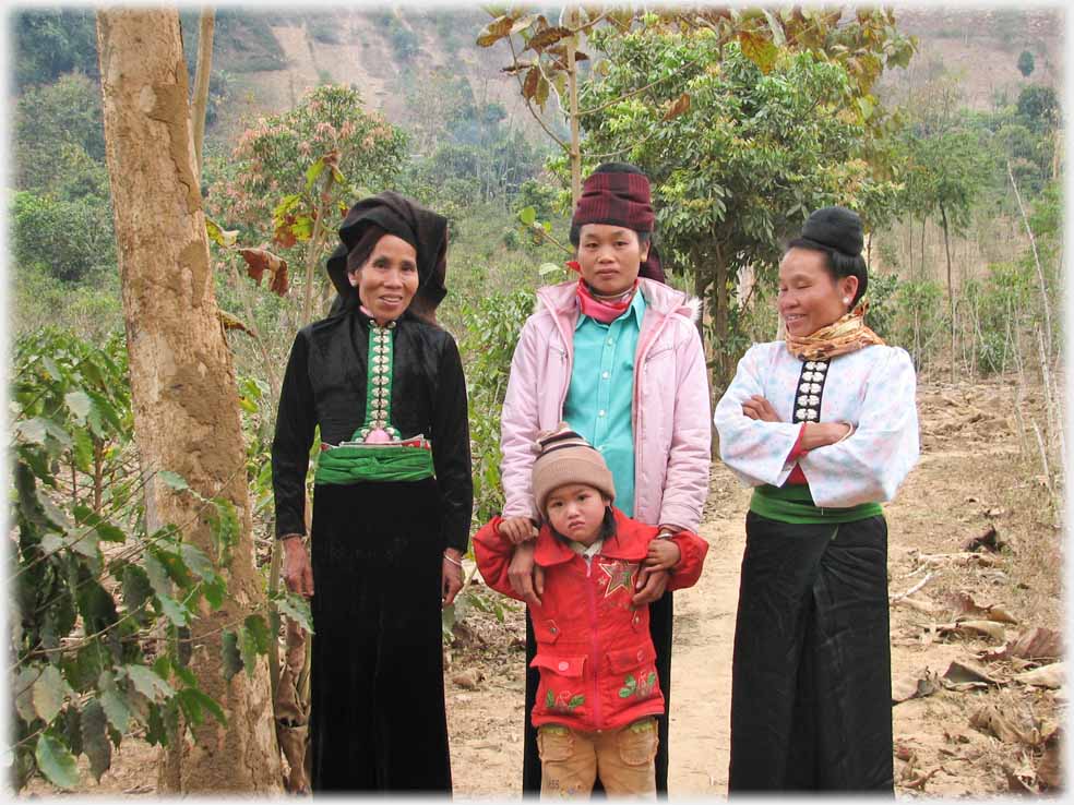 Three women and child beside coffee plants.