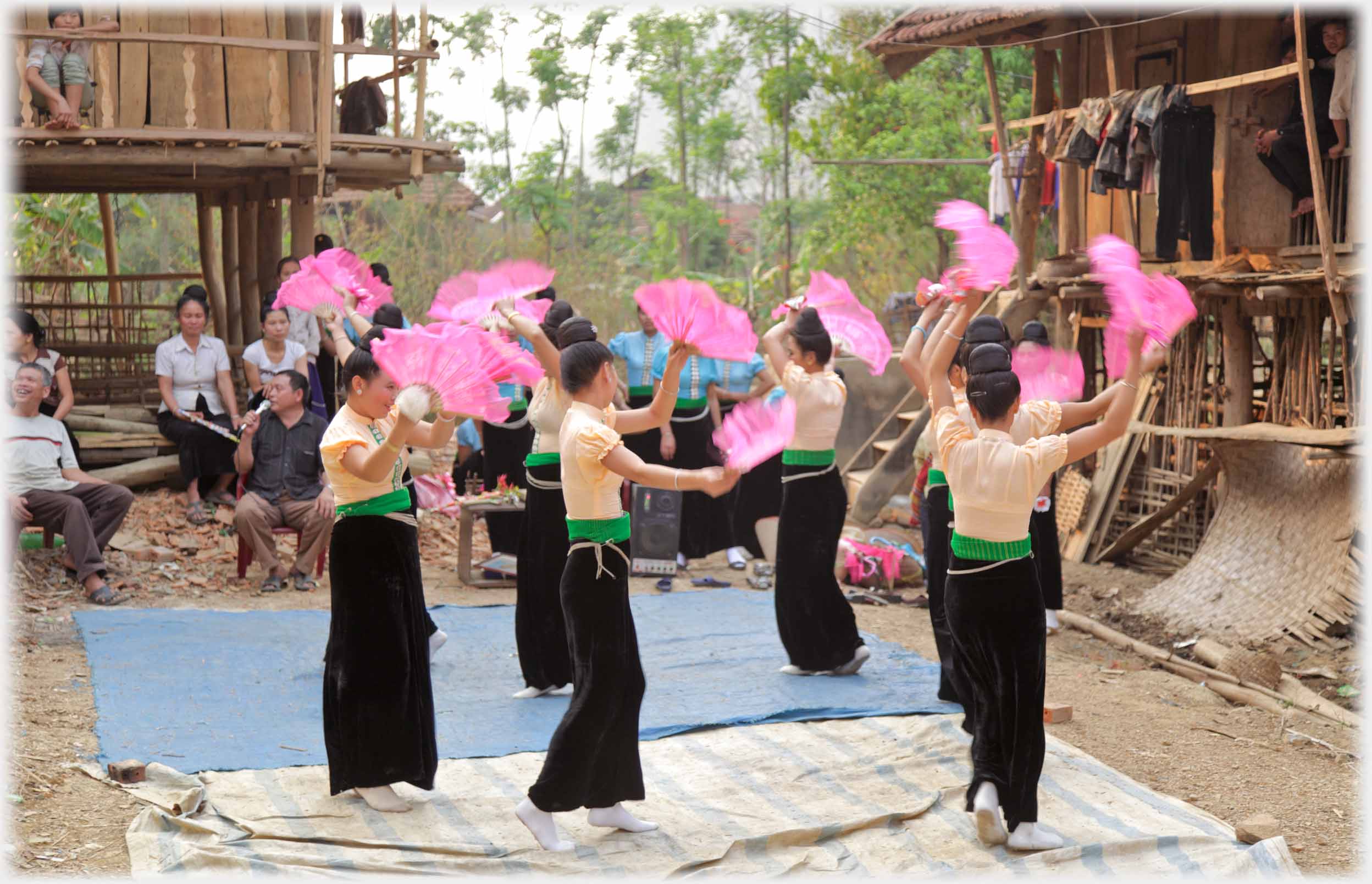 Circle of women dancing in long black skirts holding up fans.