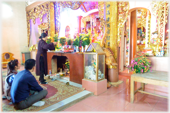 Shrine room with woman attendent and two people sitting in front of the altar.