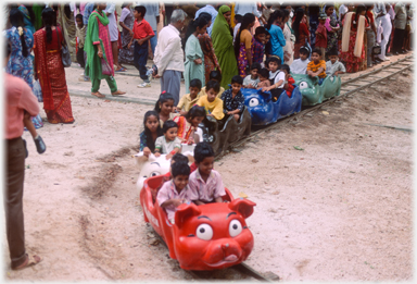People watchiing children on small coloured train.