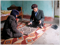 Two men playing chess on a mat with hats and coats on.