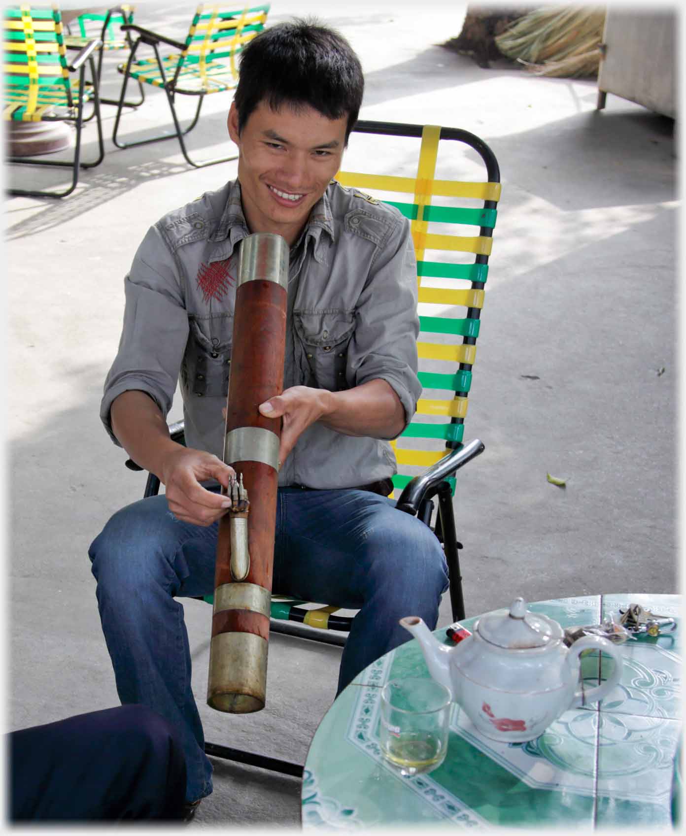Han smiling as he lights a tobacco water pipe, tea on the table.