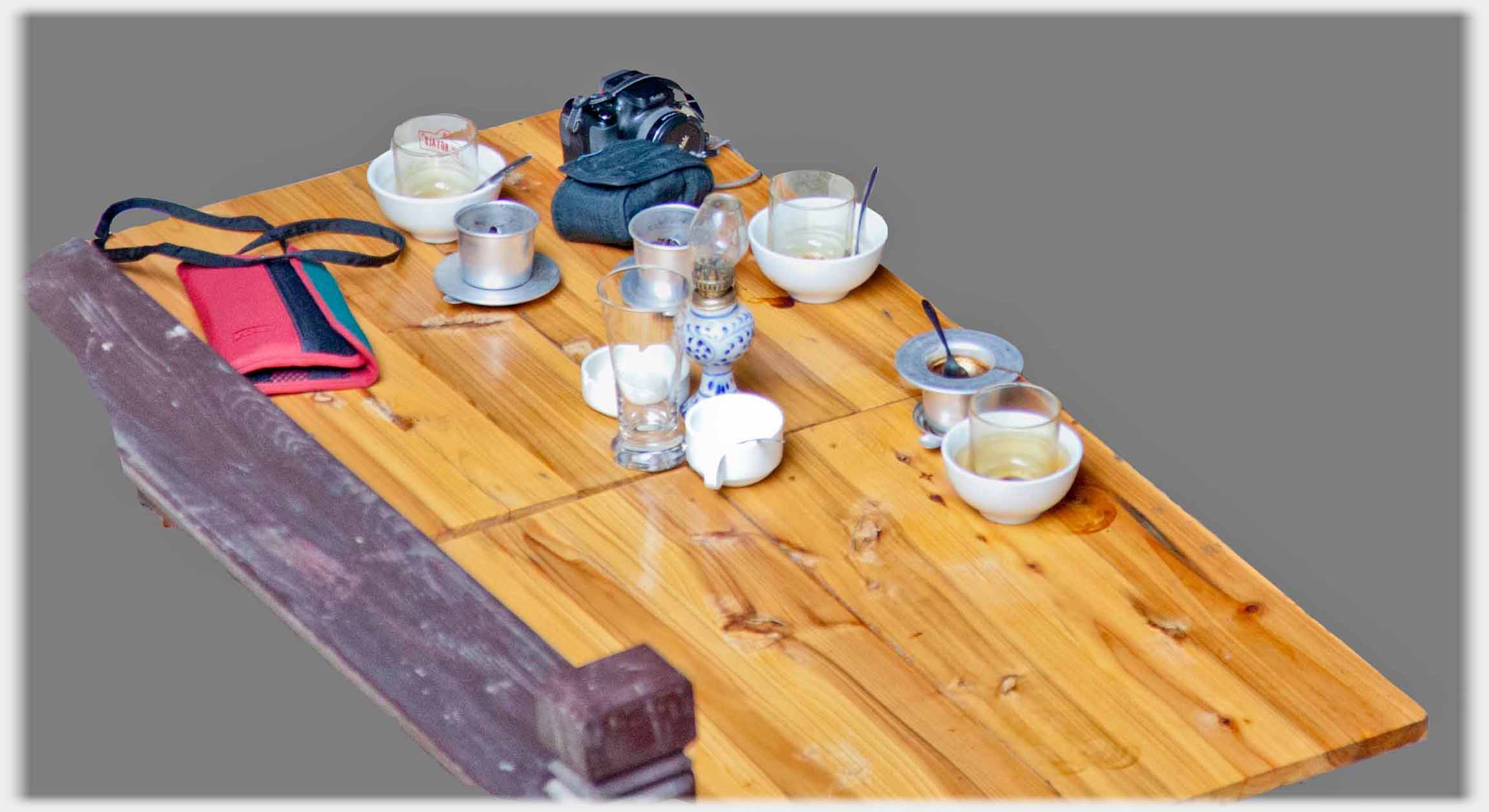 Clean wood table top with coffee filters for three, glasses, camera, purse and lamp.
