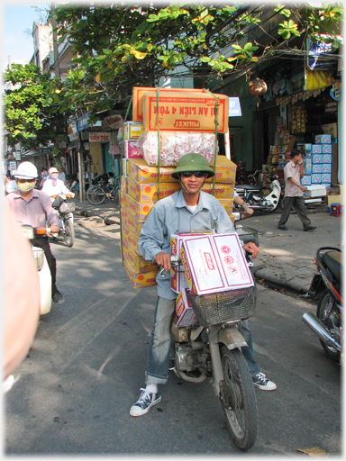 Boxes of instant noodles piled two above head of rider seen from front.