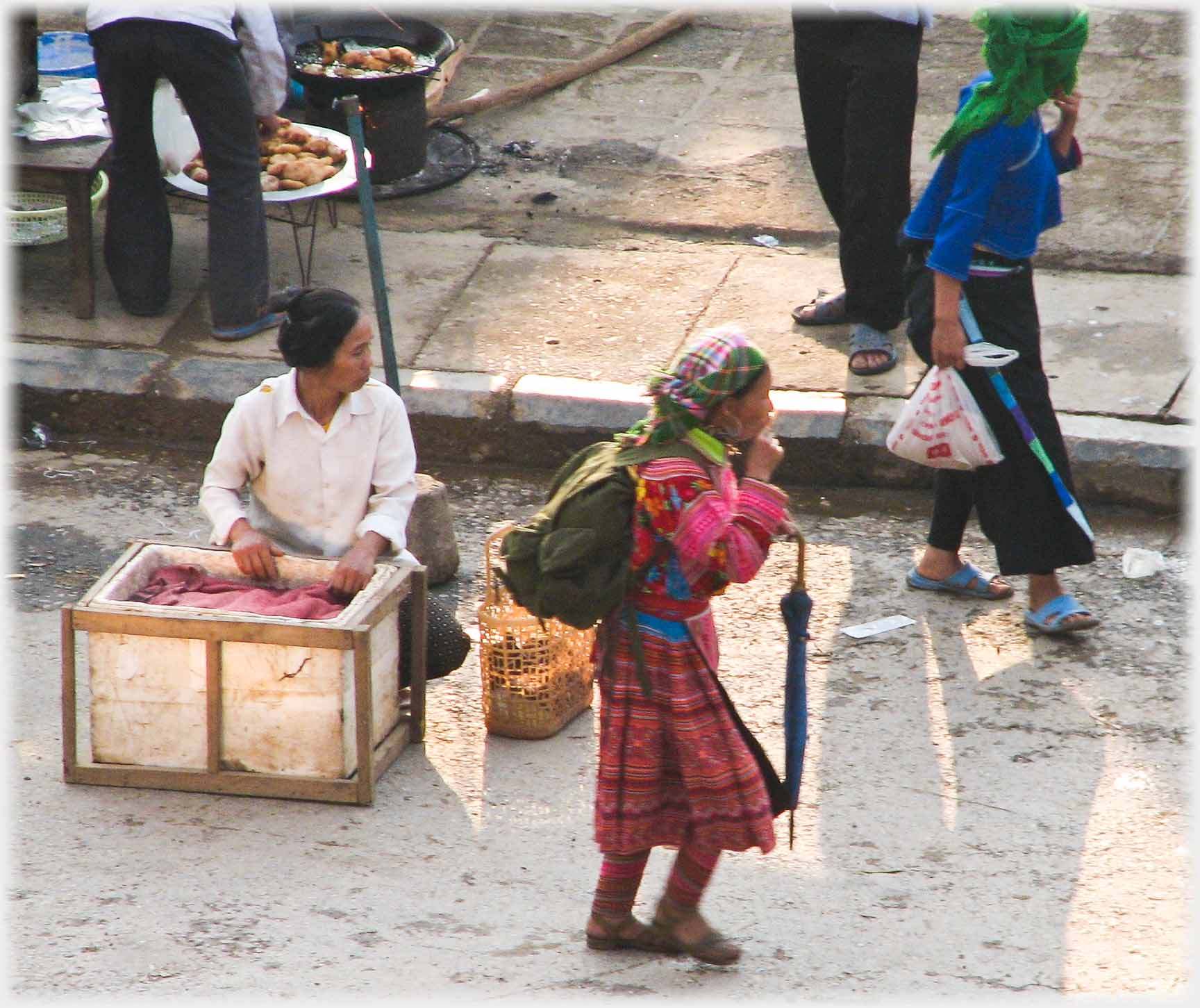 Vendor with box, older woman with umbrella passing.