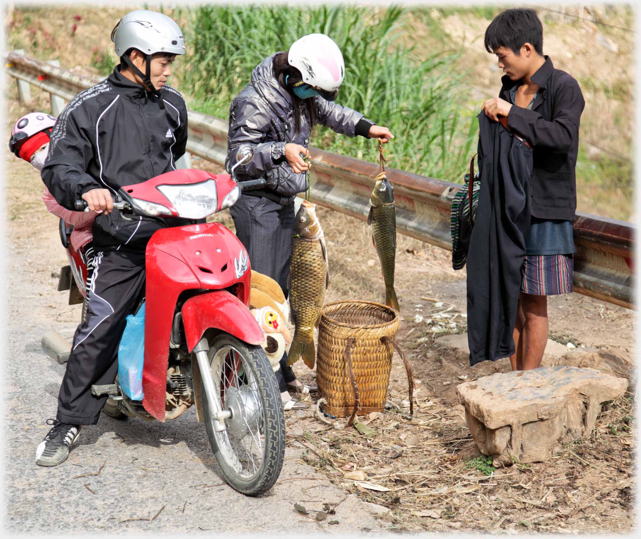 Man standing holding trousers, woman from motorbike holding two large fish.