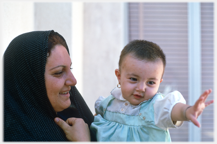 Woman holding infant with outstretched arm.