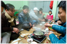 Group of people sitting around food being cooked at floor level.