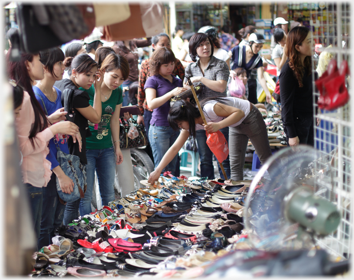 Women crowding around shop front with shoes for sale.