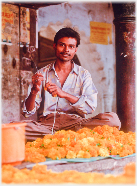 Man making garlands sitting behind pile of flowers