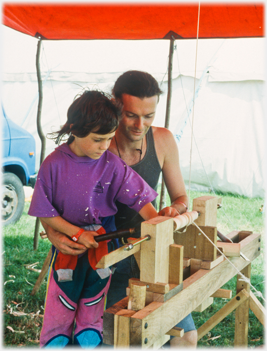 Man helping child hold chisel to lathe.