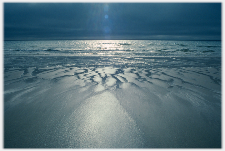 Mud flats, sea to the horizon under a setting midnight sun.