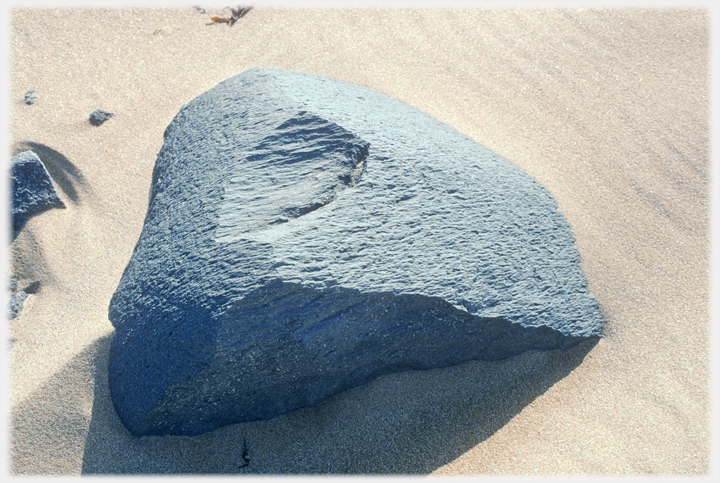 Large boulder on sand beach.