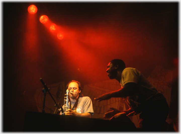 Sax player and drummer in flood lights.