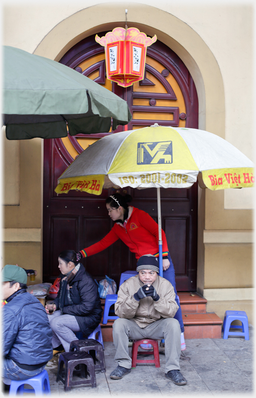 Man sitting at street cafe holding cup looking cold.