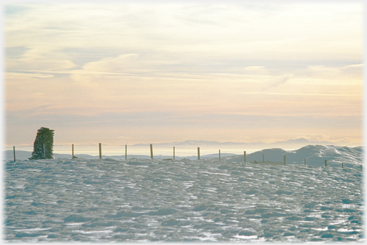 View from hilltop in snow across clouds to far hills.