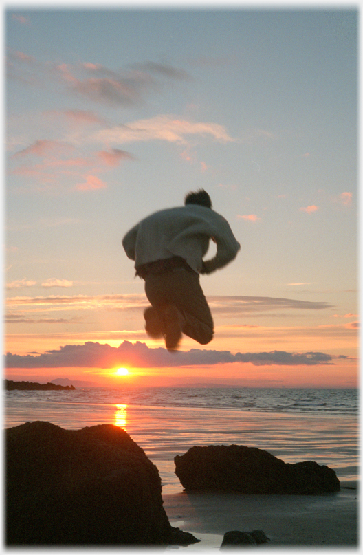Figure jumping between rocks over setting sun.