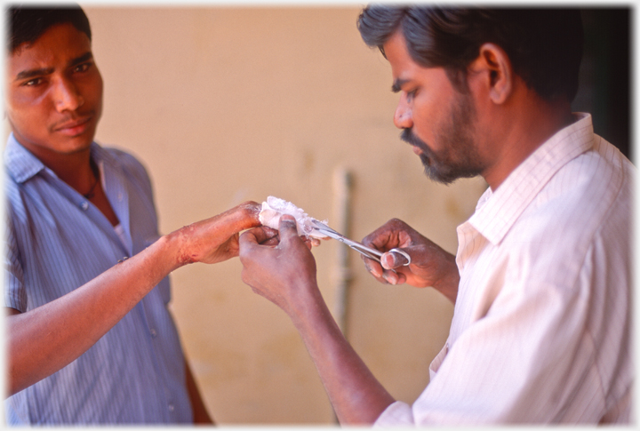 The physiotherapist Jacob removing the plaster from a young man's hand.