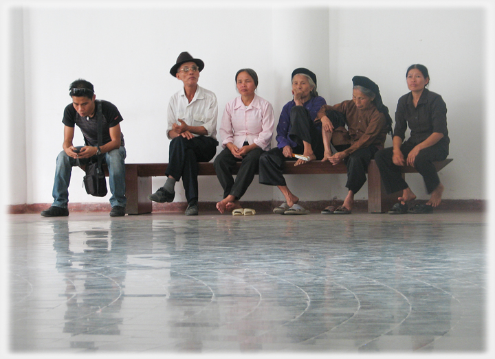 Row of people sitting on bench in large space.